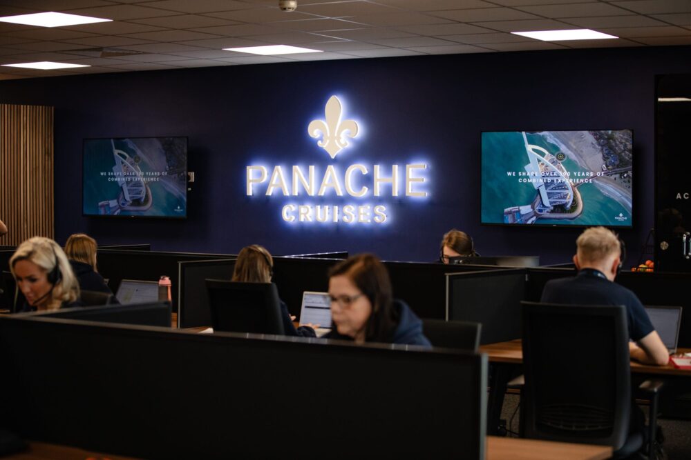 Panache Cruises’ Strawberry Fields Digital Hub, people are working on computers with a neon logo sight in the background.